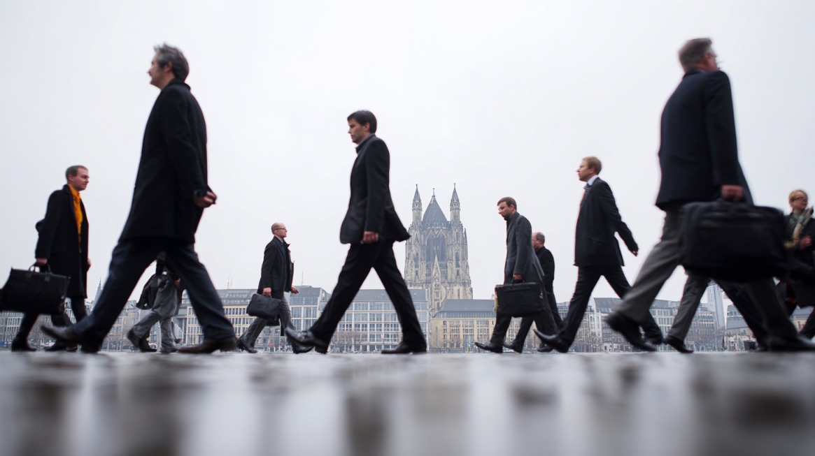 Ljudi u poslovnim odelima hodaju gradom u Nemačkoj, noseći aktovke