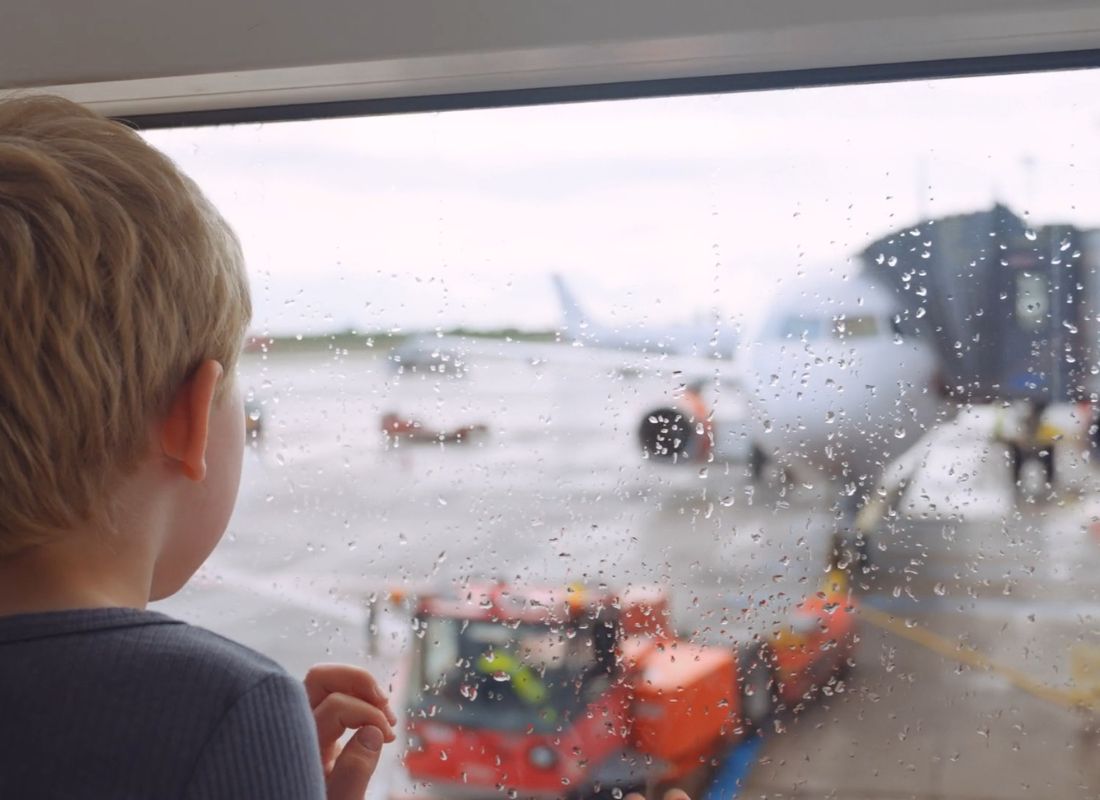 dečak na aerodromu gleda kroz prozor u avion koji se sprema za poletanje