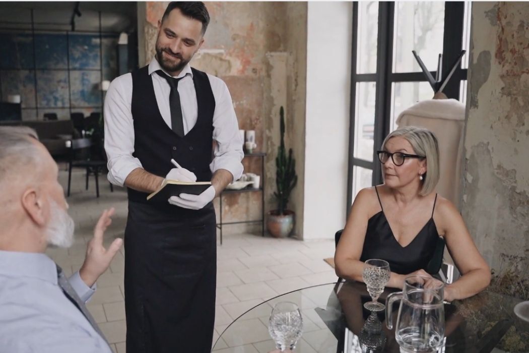 Konobar zapisuje porudžbinu dok razgovara sa gostima za stolom