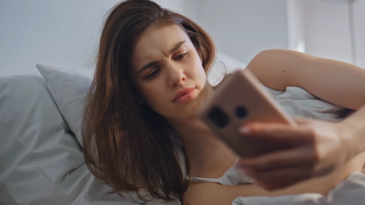 Zabrinuta žena leži u krevetu i gleda u telefon pred spavanje.